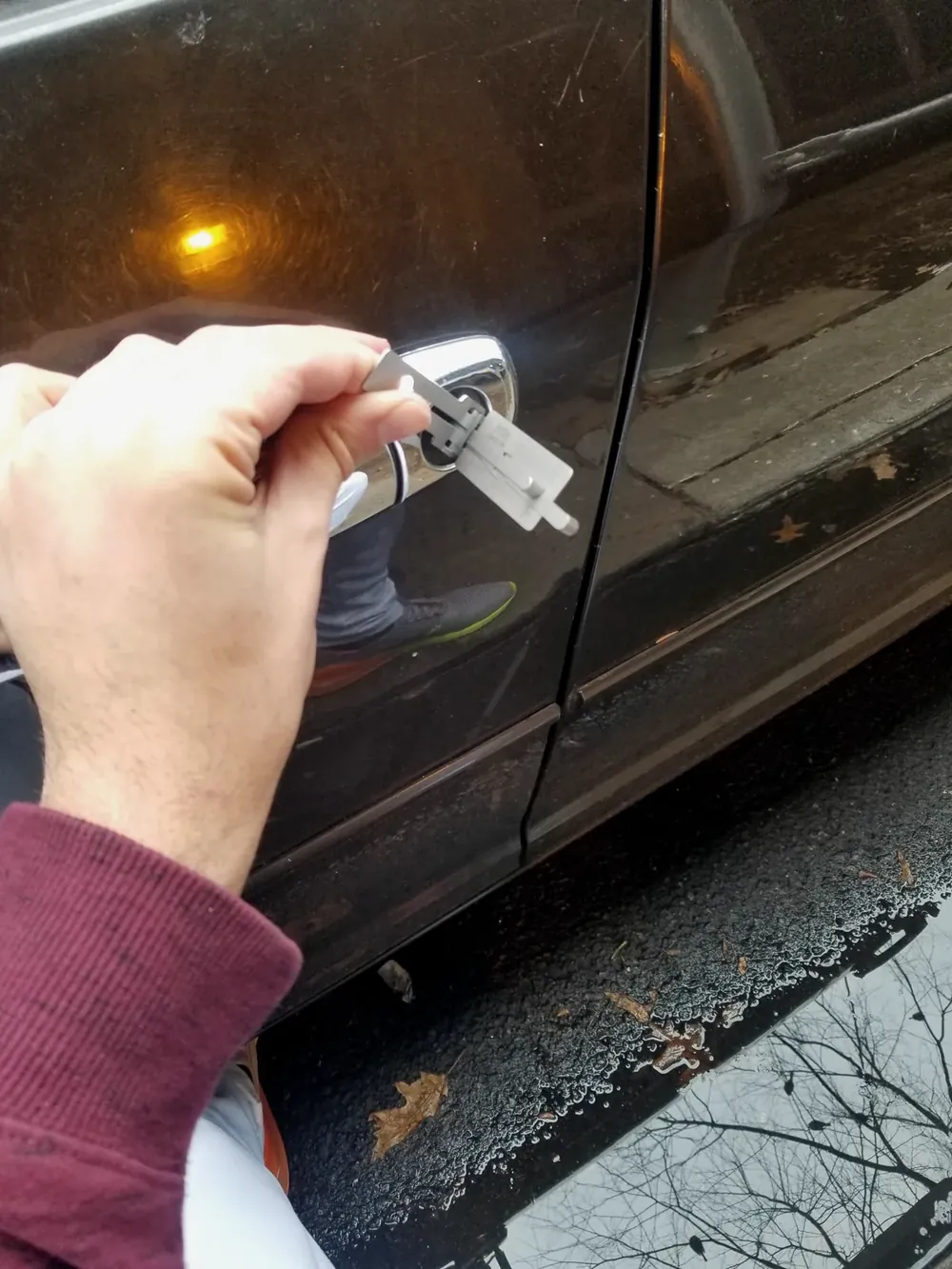 Cerrajero abriendo la puerta de un carro cerrado con una herramienta profesional